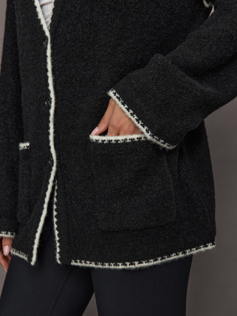 Close-up of black knit Sweater with Scarf showing front pocket and cream whipstitch edge detail.