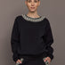 Model wearing black jewel embellished sweatshirt with crystal neckline detail, front view.