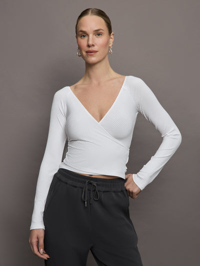 Model wears a ribbed jersey fitted long sleeved deep V neck wrapped white top with ruching down both sides. 