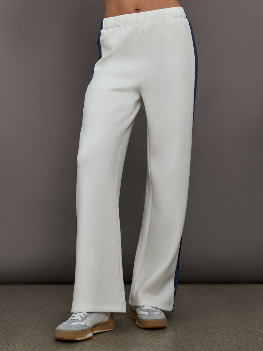Model wearing ivory wide leg track pants with blue and black stripe on the side.