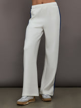 Model wearing ivory wide leg track pants with blue and black stripe on the side.