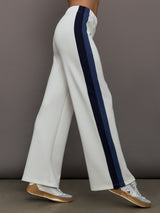 Model wearing ivory wide leg track pants with blue and black stripe on the side.