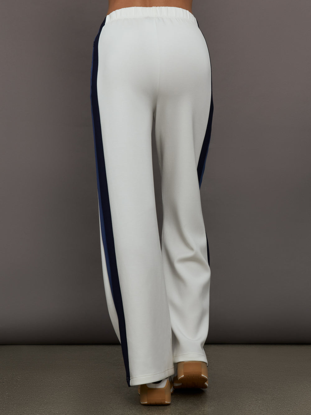 Model wearing ivory wide leg track pants with blue and black stripe on the side.