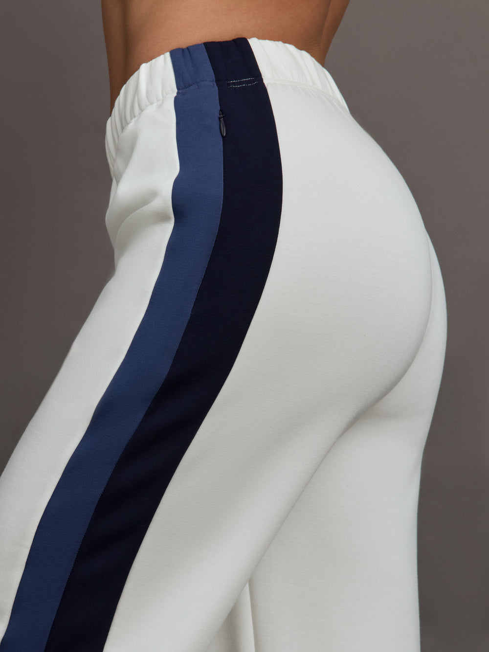 Model wearing ivory wide leg track pants with blue and black stripe on the side.