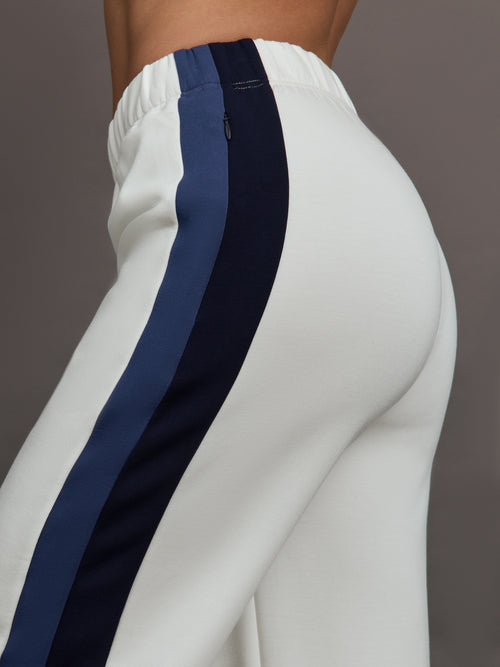 Model wearing ivory wide leg track pants with blue and black stripe on the side.