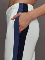 Model wearing ivory wide leg track pants with blue and black stripe on the side.