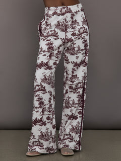 Model wears white track pants with burgundy toile print. 