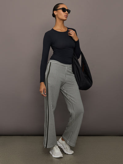 Full outfit view of houndstooth track pants styled with black ribbed top, oversized tote, and sneakers.