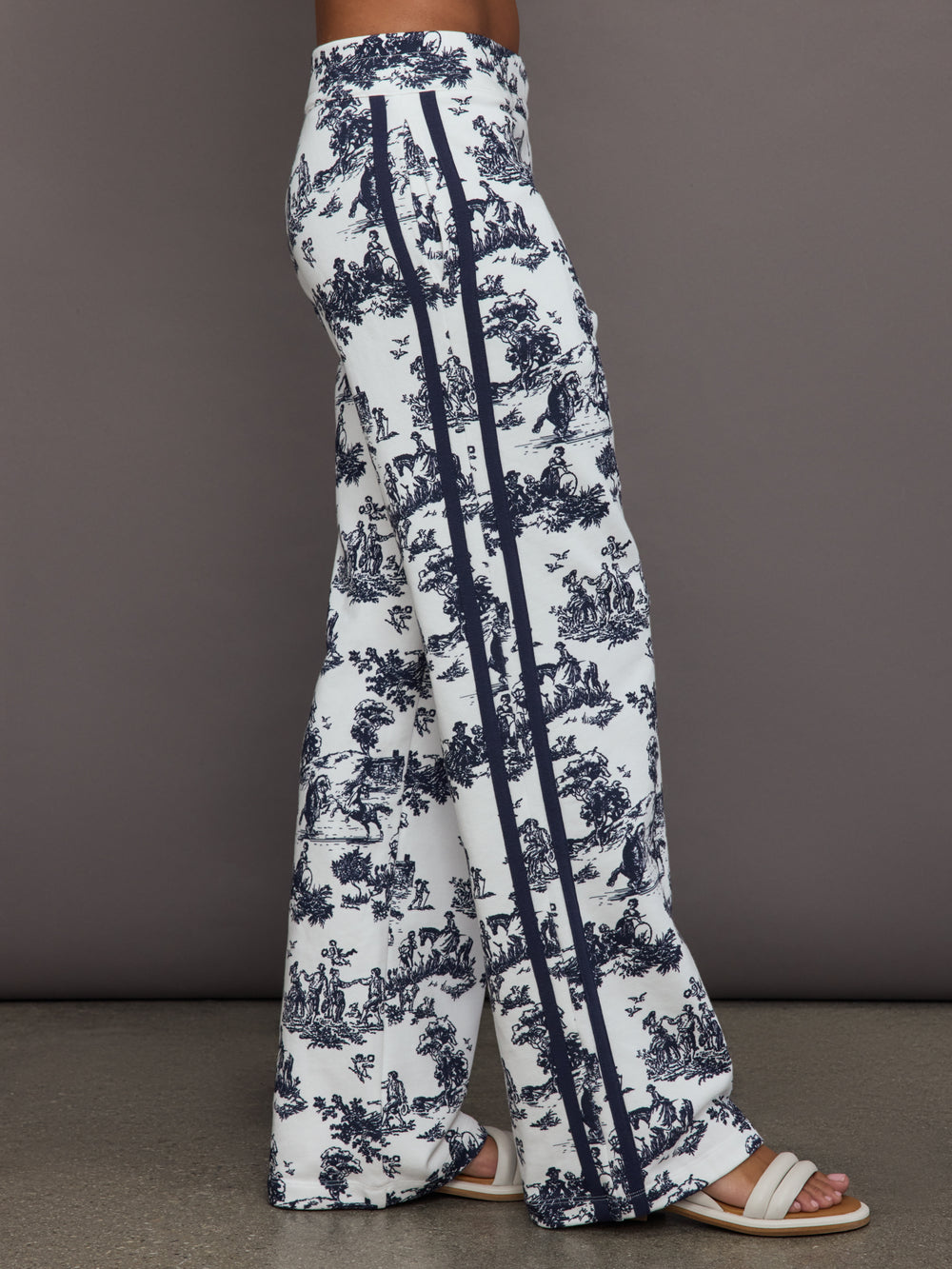 Model wears a pair of high waisted track pants in white with blue toile print and navy drawstring.