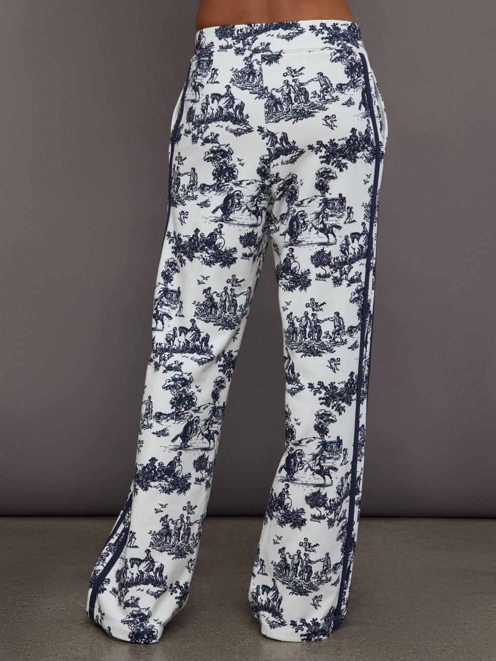 Model wears a pair of high waisted track pants in white with blue toile print and navy drawstring.