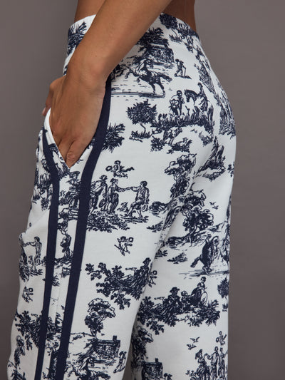 Model wears a pair of high waisted track pants in white with blue toile print and navy drawstring.