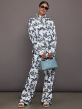 Woman wearing a white track jacket with blue floral toile pattern against a gray background.