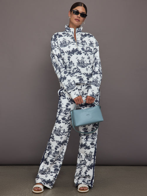 Woman wearing a white track jacket with blue floral toile pattern against a gray background.