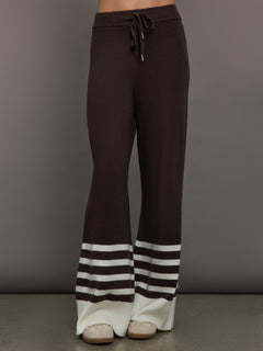 Model wears brown knit pants with white stripes on the bottom.