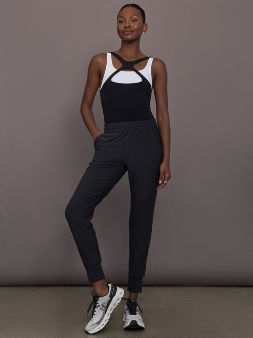 Model wears black mid rise joggers with thick ankle band.