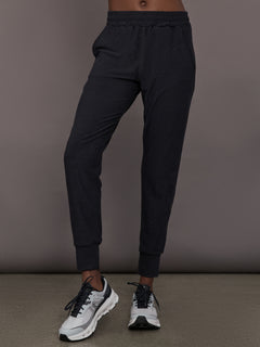Model wears black mid rise joggers with thick ankle band.