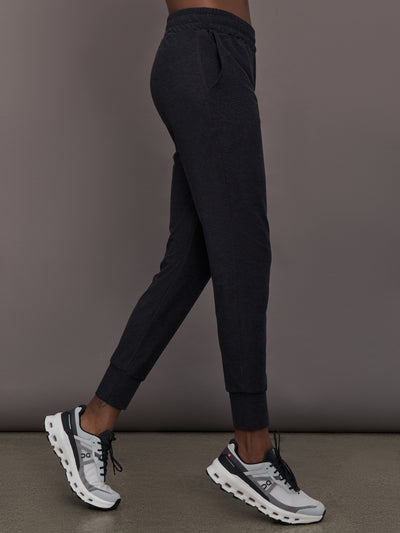 Model wears black mid rise joggers with thick ankle band.