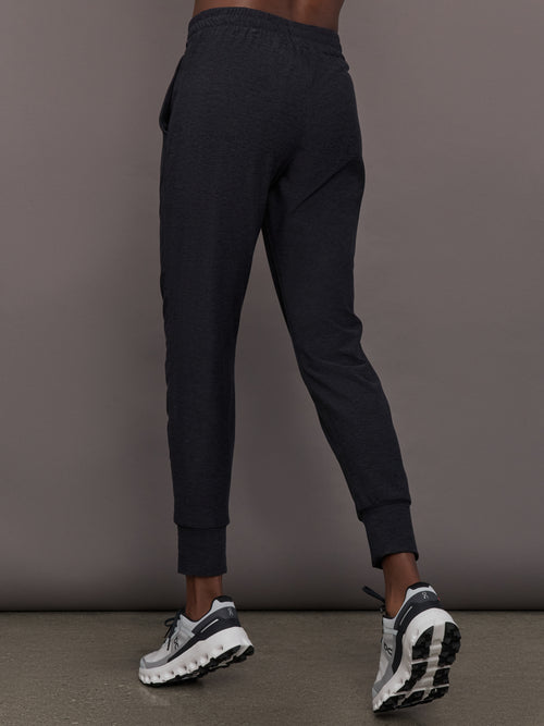 Model wears black mid rise joggers with thick ankle band.