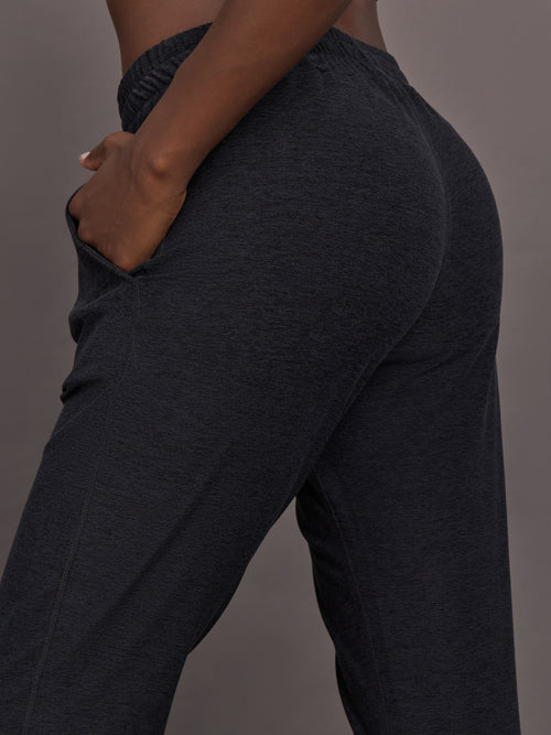 Model wears black mid rise joggers with thick ankle band.