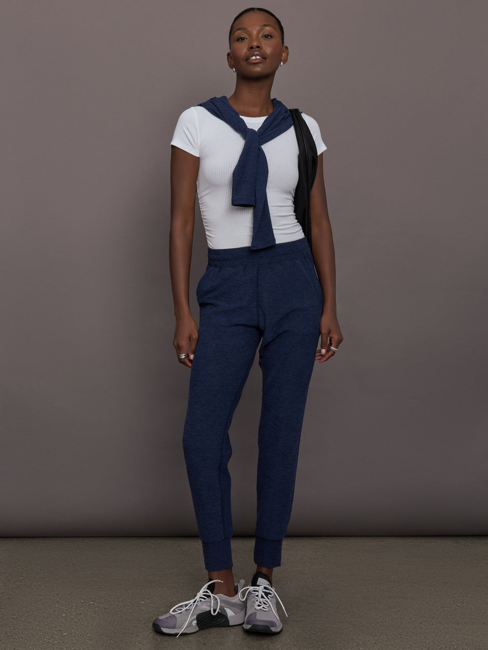 Model wears mid rise navy joggers with thick ankle band. 