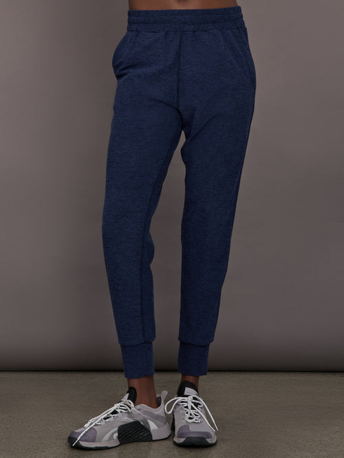 Model wears mid rise navy joggers with thick ankle band. 