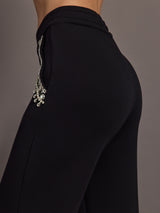 Back angle of black wide-leg pants highlighting sleek fit and jeweled pocket trim.
