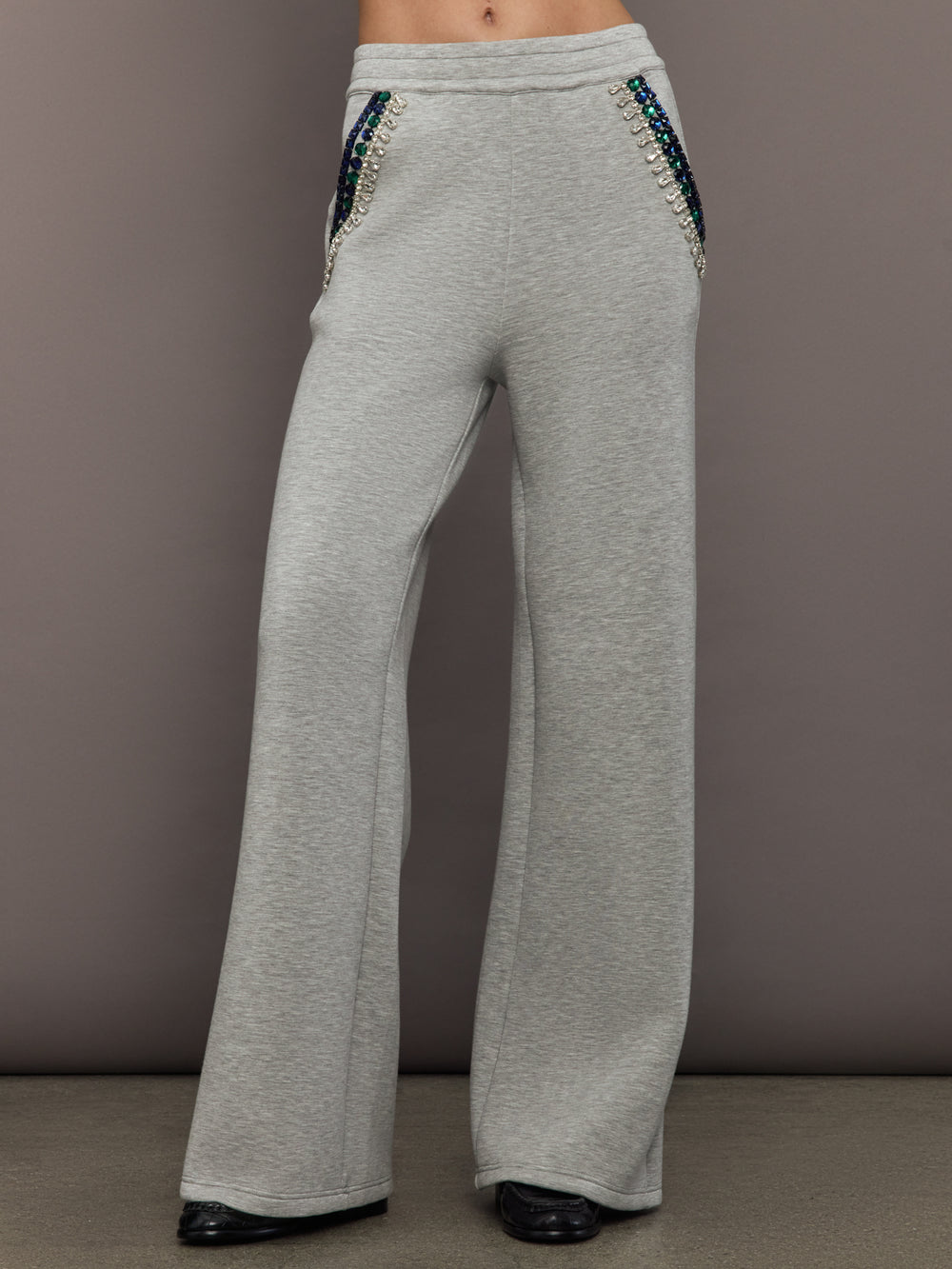 Model wearing grey wide-leg embellished pants with jeweled pocket trim, front view.