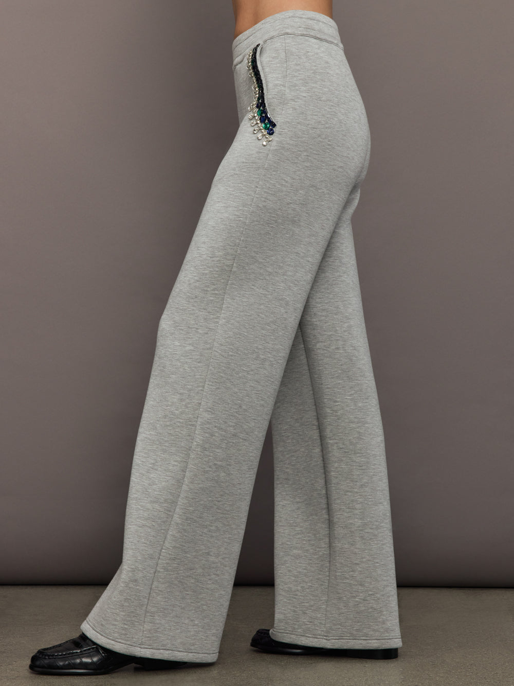 Side view of grey embellished wide-leg pants showing jeweled pocket detail and flared silhouette.