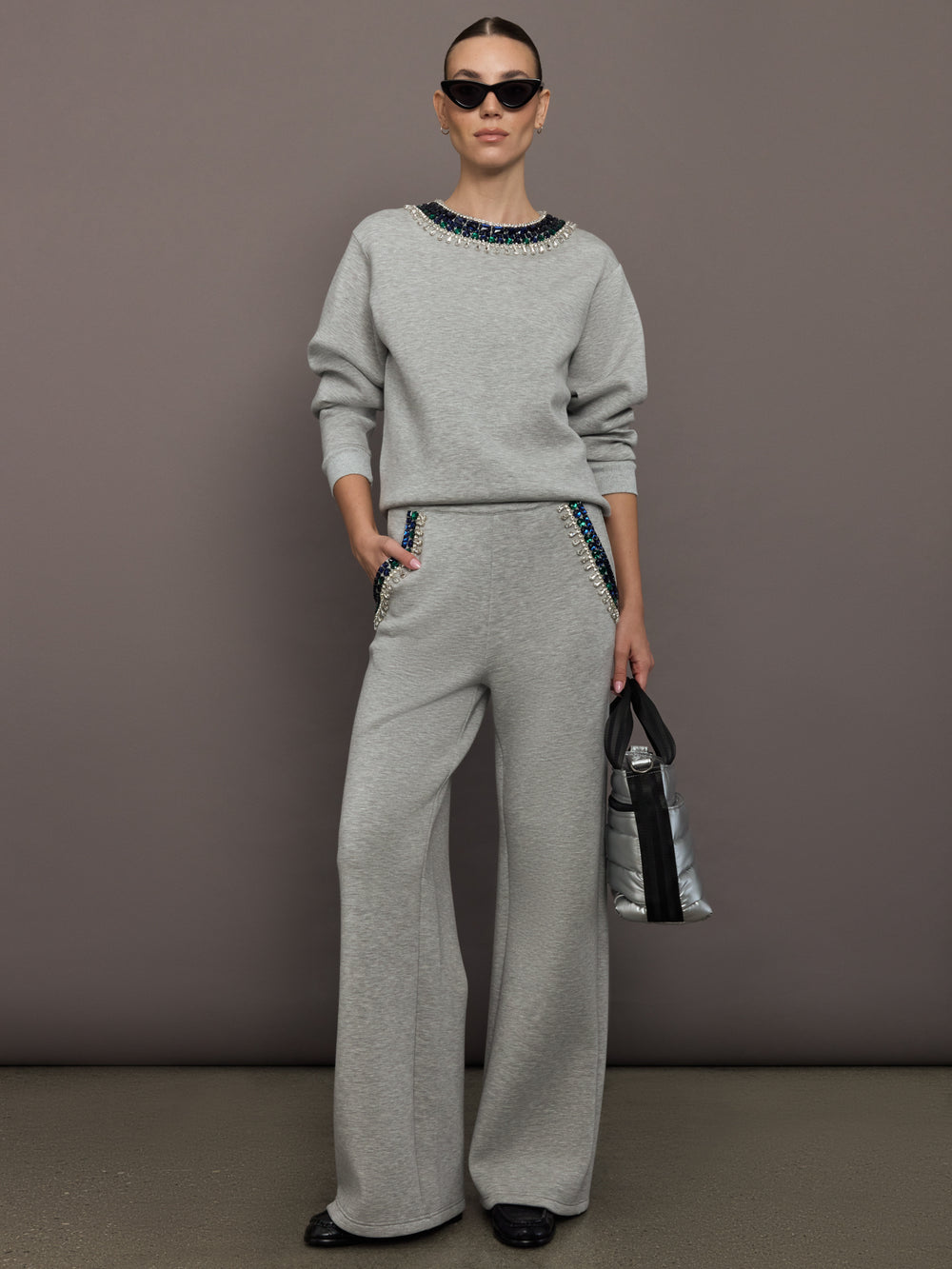 Full outfit view of grey wide-leg embellished pants styled with matching sweatshirt and green accessories.