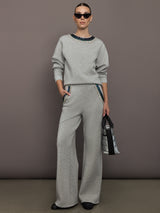 Full outfit view of grey wide-leg embellished pants styled with matching sweatshirt and green accessories.