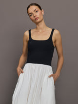 Model wears sleeveless dress with a black fitted top and white flowy bottom.





