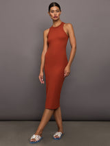 Model wears terracotta-colored, ribbed tank dress with a high neckline, sleeveless design, and a slim, body-hugging fit that extends right below the knee.