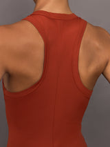 Model wears terracotta-colored, ribbed tank dress with a high neckline, sleeveless design, and a slim, body-hugging fit that extends right below the knee.