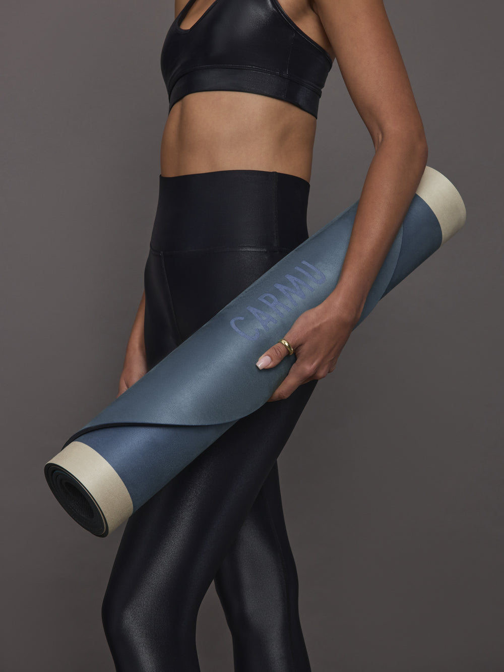 Model in black activewear holding rolled Navy Aeris yoga mat in Navy and Blue with CARMU logo visible.