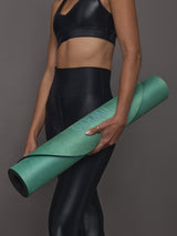Model in black activewear holding rolled Teal Gradient yoga mat with CARMU logo visible.