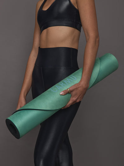Model in black activewear holding rolled Teal Gradient yoga mat with CARMU logo visible.