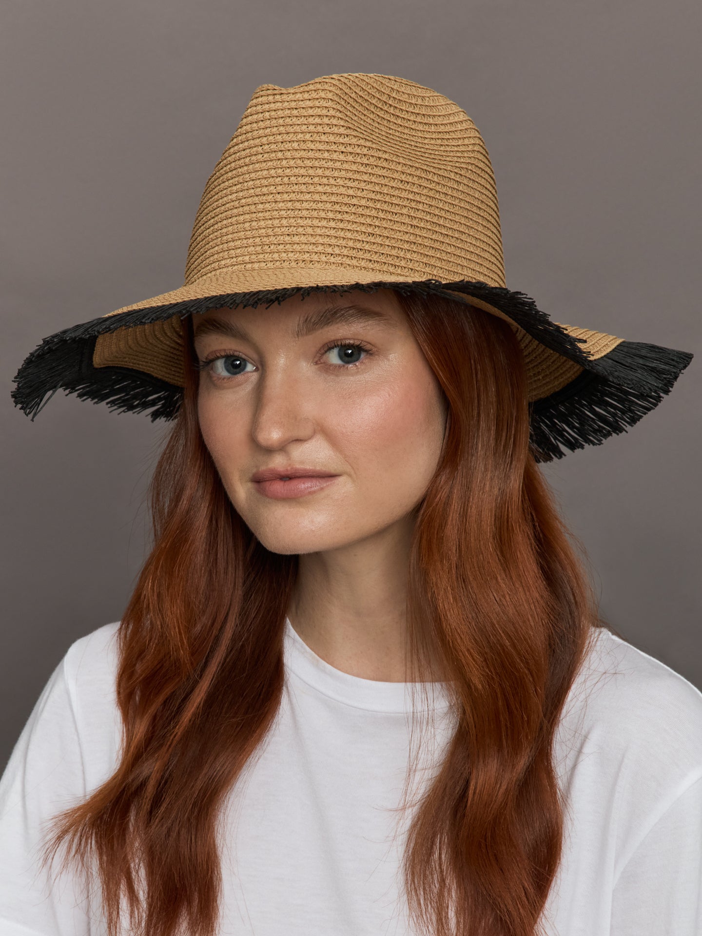  Model wears a caramel-colored straw fedora with a fringed black edge.