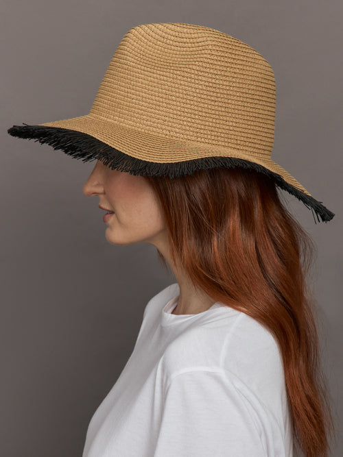  Model wears a caramel-colored straw fedora with a fringed black edge.