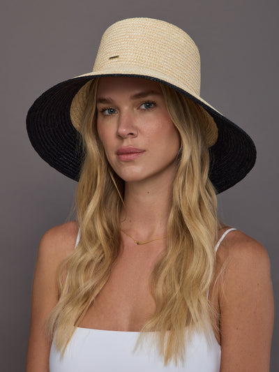 Model wearing ivory wide-brim straw sun hat with black brim, front view.