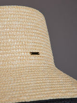 Close-up of ivory straw hat texture with black brim and logo detail.