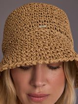 Close up of crochet bucket hat in camel showing the woven texture and logo plate.