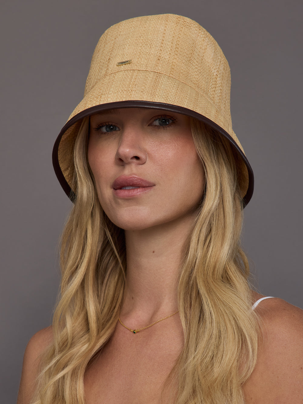 Front view of model wearing natural woven straw bucket hat with dark contrast trim.