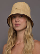 Front view of model wearing natural woven straw bucket hat with dark contrast trim.