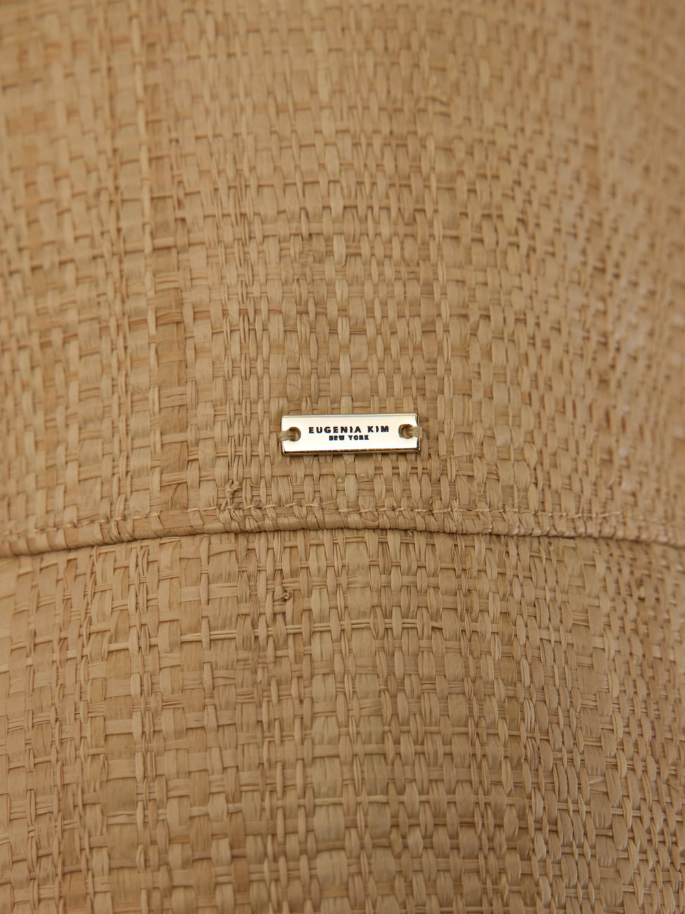 Close-up of woven straw bucket hat with logo plaque detail.