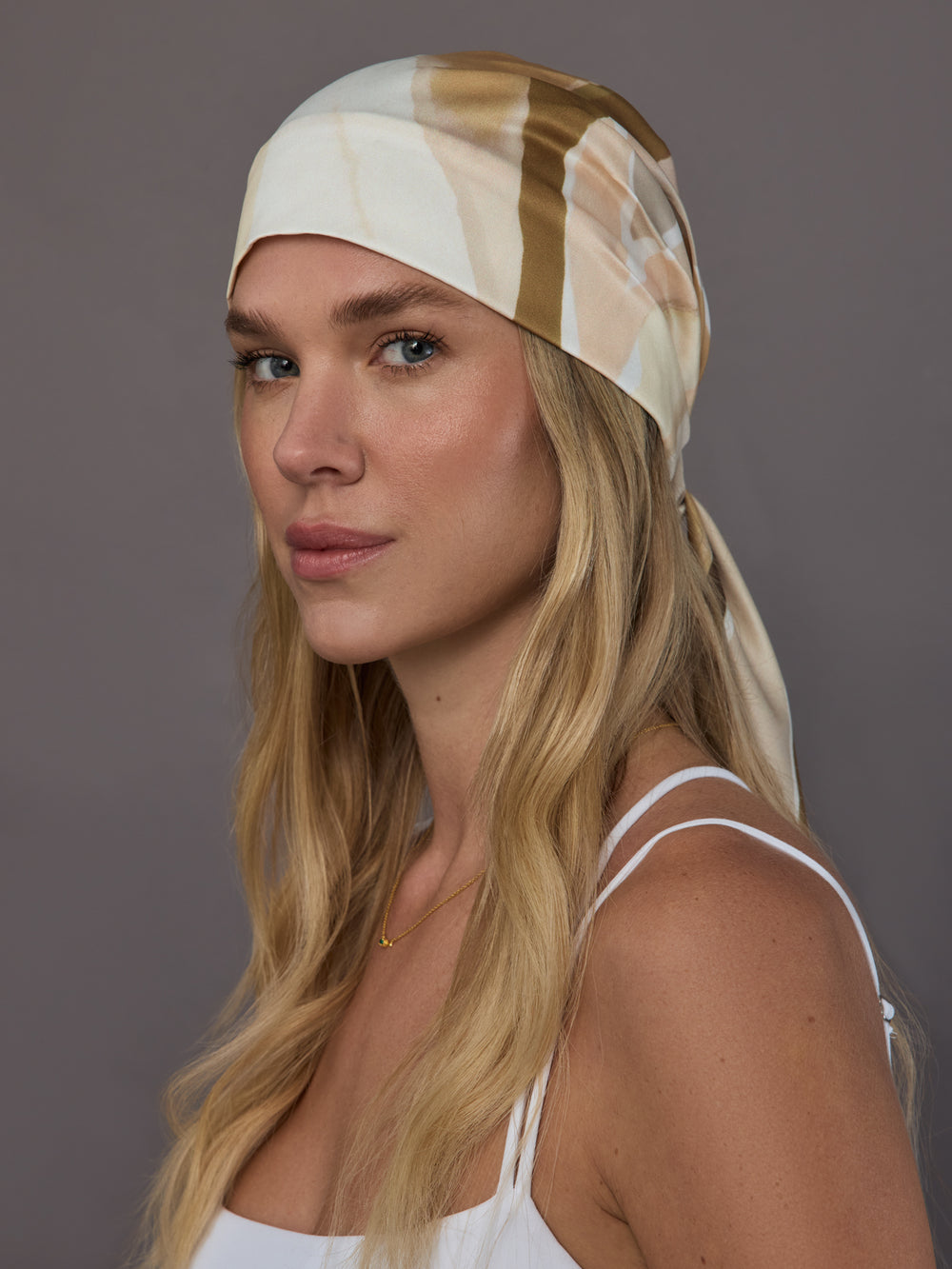 Front angle view of model wearing ivory neutral printed silk headscarf tied at back.