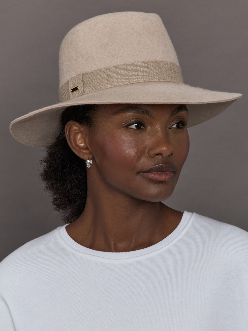 Model wearing a beige hat against a gray background