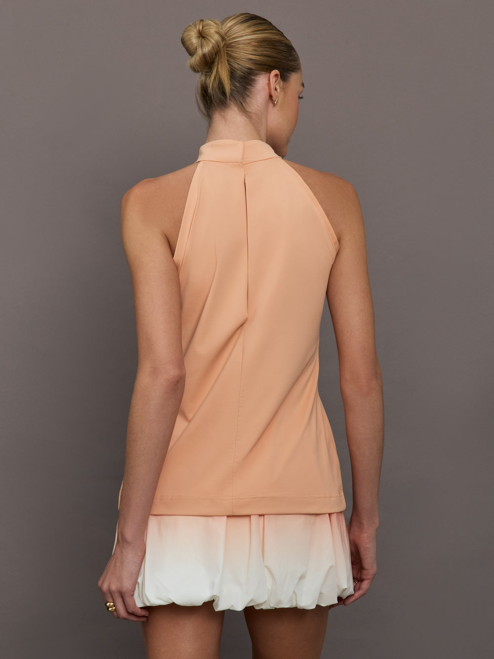 Model is wearing a peach mock neck halter top and skirt against a plain background.