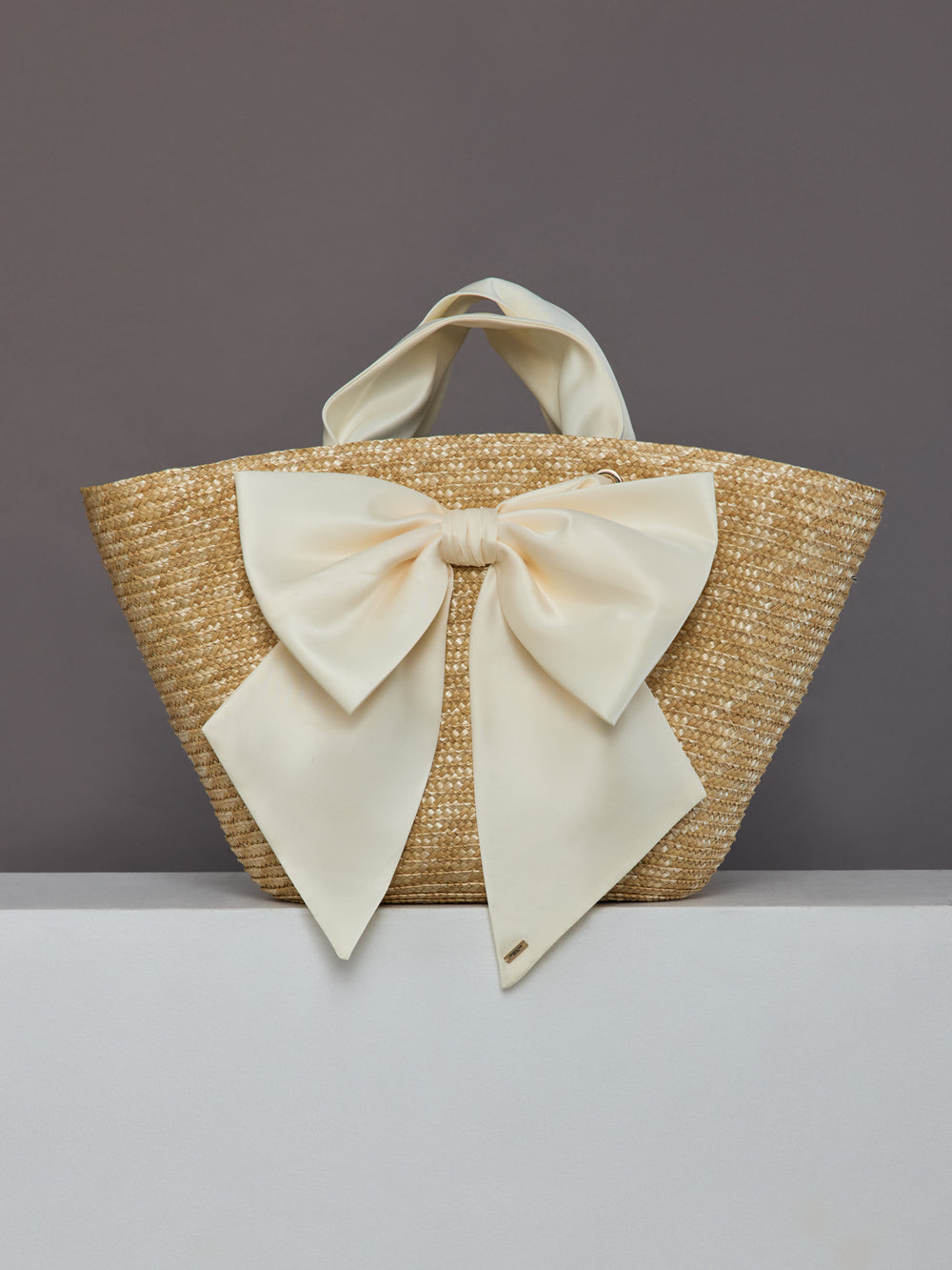 Front view of oversized straw tote with large ivory satin bow.