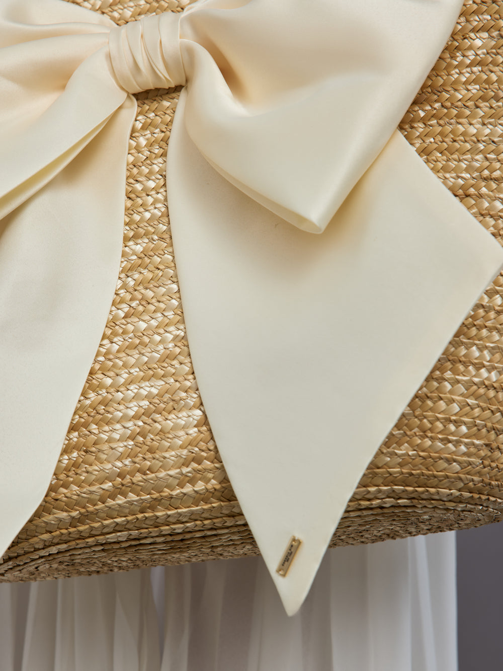 Close-up of ivory satin bow detail on natural straw tote bag.