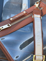 Clear vinyl crossbody pouch with brown leather trim, gold zipper, and Fenix Sportier logo strap outdoors.